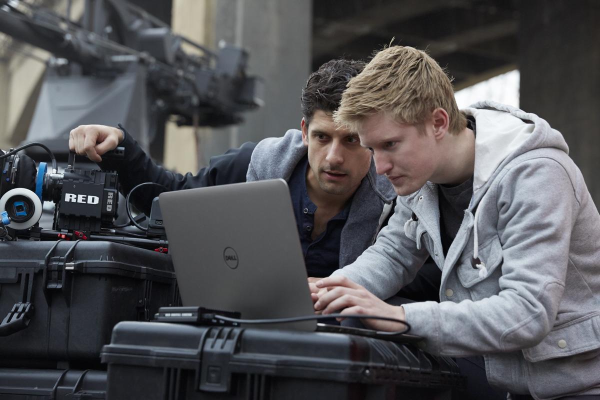 Two Men on a film set using a Dell Precision M3800 Mobile Workstation and a Red digital cinema camera, with a crane and bridge in the background.